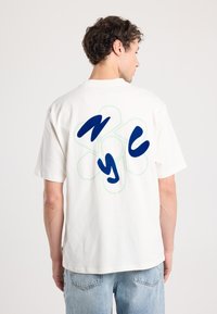 White cotton T-shirt featuring a large blue "NYC" design with a green outline on the back. Short sleeves, relaxed fit, and crew neckline.
