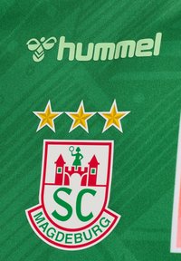 Groene sporttrui met het "hummel" logo in lichtgroen. Bevat een rood en wit schildlogo met drie sterren erboven en de tekst "SC Magdeburg".