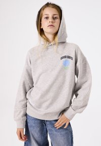 Sudadera de felpa gris con un gráfico en el frente que dice "BUENOS DÍAS", cuenta con un gran bolsillo canguro y puños acanalados. Combinada con jeans azules.