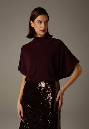 Burgundy knit top with a high neck, short sleeves, paired with a fitted black sequined skirt that reflects light and adds texture.
