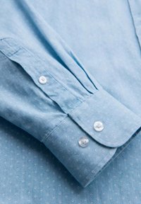 Lichtblauw button-up shirt met een subtiel geometrisch patroon, lange mouwen en witte knopen op de manchetten, gemaakt van zachte stof.