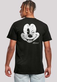 Juodas medvilnės marškinėliai su dideliu, nudėvėtu baltu Mickey Mouse grafiką nugarėlėje. Trumpomis rankovėmis ir klasikiniu siluetu.