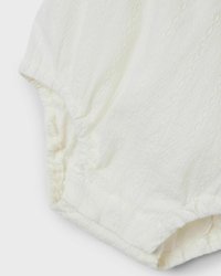 Romper bianco con texture, realizzato in un morbido tessuto plissettato con motivi delicati. Inserto elastico aderente attorno alle gambe e alle spalle.