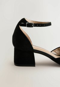 Sandale à talon en daim noir avec un talon carré, une bride de cheville et un détail boucle. Doublure intérieure lisse et design à bout ouvert.