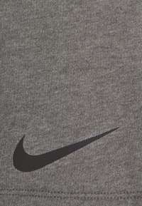 Grått tyg med en texturerad stickning, med en framträdande svart Nike swoosh-logotyp placerad i nedre högra hörnet.