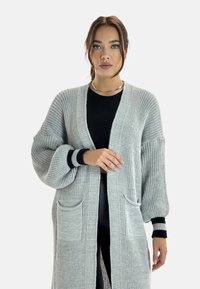 Cardigan lungo e aperto davanti in tessuto a maglia grigio chiaro. Presenta polsini a coste e due tasche frontali. Motivo testurizzato su tutta la superficie.