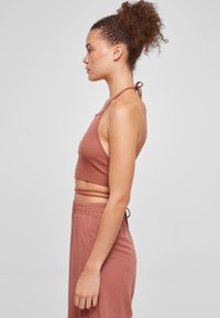 Rustfarget ribbet crop top med halterneck-bånd, med et tettsittende design. Kombinert med matchende høyt midje bukser. Glatt tekstur.