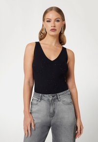 Must mustriga bodysuit V-kaelusega ja hõbedaste kaunistustega, koos tuhmide hallide k�õrge vöökohaga teksadega. Sile tekstuur.