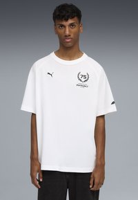 Biała bawełniana koszulka z krótkimi rękawami raglanowymi. Posiada czarny logo z napisem "75" i "Formula 1" na klatce piersiowej oraz logo Pumy na rękawie.