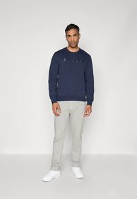 Sudadera azul marino con logo bordado, combinada con pantalones deportivos gris claro y zapatillas blancas, con un corte relajado y puños acanalados.