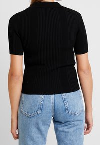 Svart ribbad top med korta ärmar och krage, med en figurnära design och strukturerat mönster. Kombineras med ljusblå högmidjade jeans.