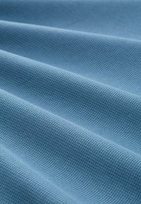 Baumwollstoff in Hellblau mit einem strukturierten, gewebten Muster, das subtile Rillen und unterschiedliche Tiefen an der Oberfläche aufzeigt.