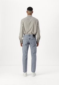 Camisa de botones gris claro de manga larga, combinada con jeans de cintura alta azul claro. Zapatillas blancas y una etiqueta negra visible en los jeans.