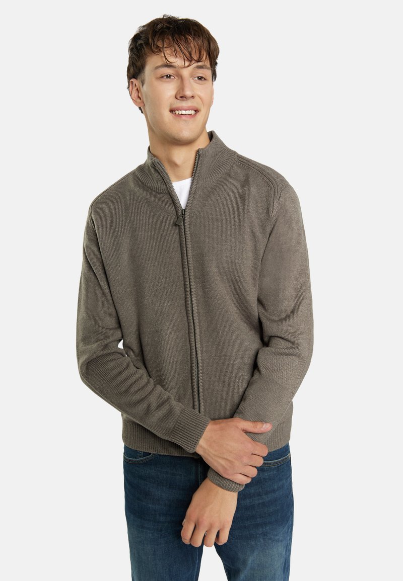 Maglione con zip davanti in maglia a coste color taupe, presenta un colletto alto e polsini aderenti, abbinato a jeans in denim blu.