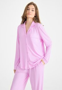Ljusrosa pyjamasset gjort av mjukt tyg, med långa ärmar, knäppning framtill och en bröstficka, samt avslappnade byxor.