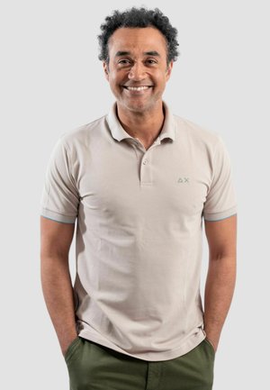 Polo shirt beige chiaro con maniche corte, caratterizzato da un piccolo logo verde sul petto e dettagli blu ai bordi delle maniche.