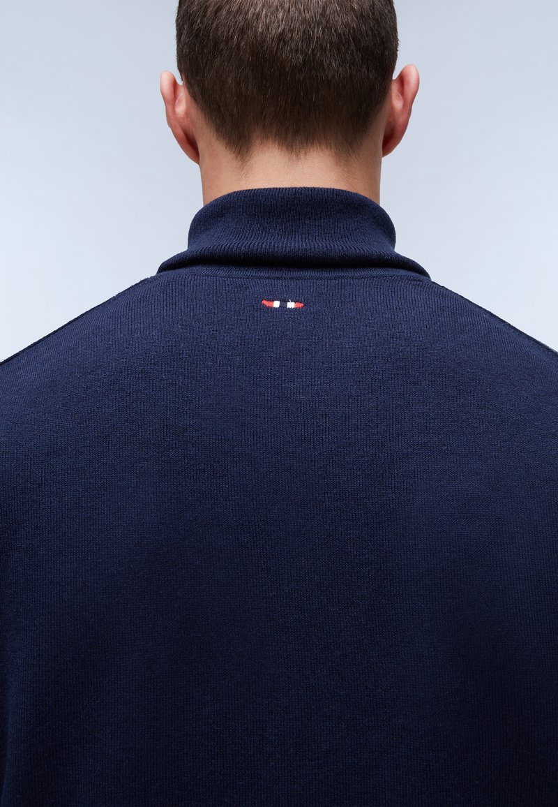 Pullover blu navy con colletto alto, caratterizzato da un piccolo logo ricamato in rosso, bianco e blu sul retro. Tessuto dalla consistenza liscia.
