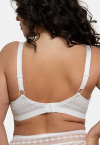 Soutien-gorge en dentelle blanche avec des motifs géométriques, bretelles réglables, fermeture à crochets et œillets, et finition en dentelle douce à bords festonnés.