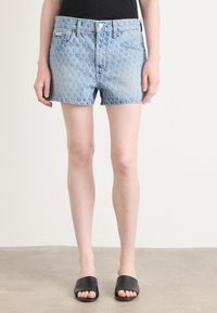 Lyseblå denimshorts med et subtilt mønster, fem lommer, knappelukking foran og råkant, parret med svarte sandaler.