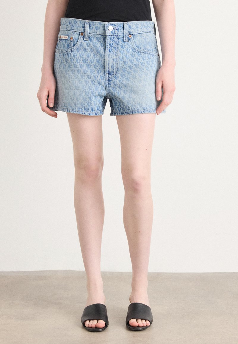 Lyseblå denimshorts med et subtilt mønster, fem lommer, knappelukking foran og råkant, parret med svarte sandaler.