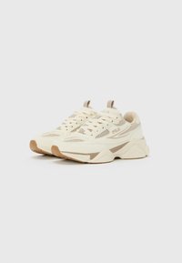 Et par beige FILA-sneakers med mesh-paneler, semsket detaljer og robuste såler på en hvit bakgrunn.