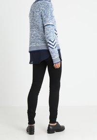 Suéter de punto en tonos azules con patrón texturizado y acentos de chevrón, combinado con pantalones negros ajustados y zapatos negros.