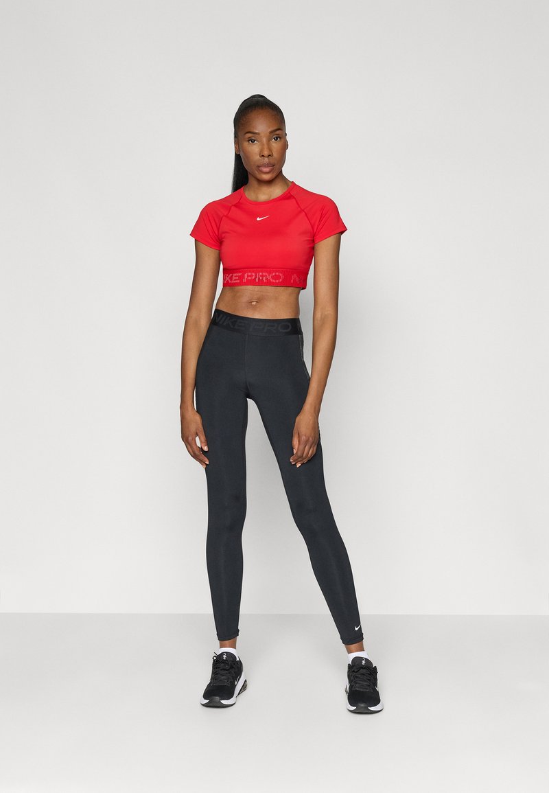 Red cropped athletic top with a white logo, paired with black leggings featuring a branded waist. Black sneakers complete the outfit.