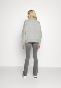 Suéter cinza com colarinho alto, ombros caídos e bainha canelada. Usado com jeans cinza de corte flared e ténis brancos. Textura suave.