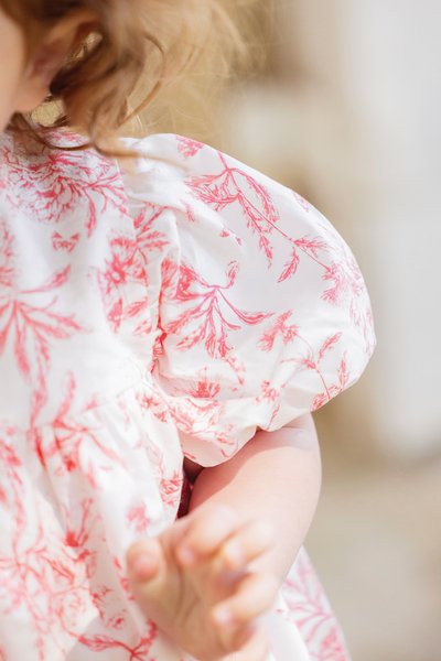 Vit blus med rosa blommönster, puffärmar och samlad midja. Lättviktig bomullsstoff med en slät textur.