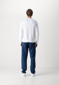 Vit sweatshirt med rund halsringning, i kombination med blå löst sittande jeans. Jeanssen har klassiska fickor och en något strukturerad yta.