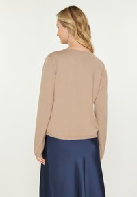 Maglione beige leggero con maniche lunghe e scollatura rotonda, che presenta una texture liscia. Abbinato a una gonna di raso blu navy.