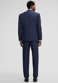 Marineblauer Anzug mit taillierter Passform, bestehend aus einer einreihigen Jacke und einer gerade geschnittenen Hose. Weicher Stoff, minimale Details und keine Muster.