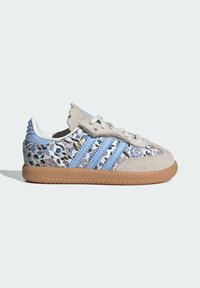 Baskets Adidas pour enfant en daim beige, tissu floral bleu, rayures bleu clair, lacets blancs et semelle en gomme sur fond blanc.