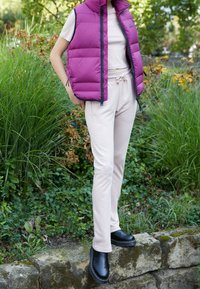 Lila pufferväst, ljusbeige t-shirt och matchande joggers med sidobrodyr. Svarta ankelstövlar fulländar outfiten.