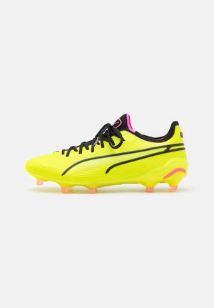 Scarpe da calcio gialle con accenti neri, lati in rete e dettagli rosa. Presentano un design elegante e sei tacchetti rotondi rosa sulla suola.