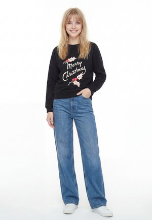 Zwarte sweatshirt met de tekst 'Merry Christmas' en hulstprint, gecombineerd met lichtblauwe wijde jeans en witte sneakers.