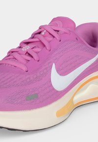 Gros plan sur une chaussure de course Nike rose avec logo swoosh blanc, lacets roses et semelle beige avec détail orange.