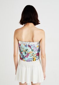 Bandloze top met een blauwe geborduurde bloemenmotief en kleurrijke pailletten. Witte rok met uitlopende stijl en sierdetails van kralen aan de taille.