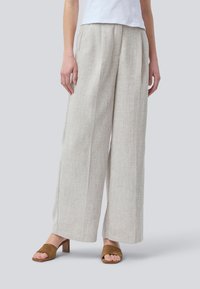 Pantaloni a gamba larga color beige chiaro realizzati in tessuto testurizzato, con pieghe frontali e vestibilità ampia, abbinati a sandali con tacco in suede marrone.