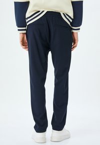 Pantalones jogger en color navy con cintura elástica, dos bolsillos traseros y perneras ajustadas. Tejido suave con una textura lisa. Combinados con zapatillas blancas.