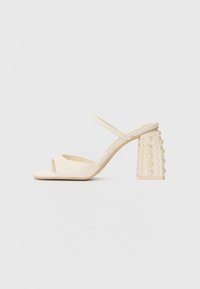 Sandales à talons ouverts beiges avec une finition satin lisse, dotées d'un talon bloc orné d'accents ronds ressemblant à des perles.