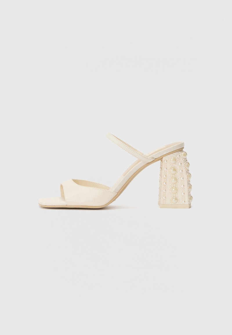Sandales à talons ouverts beiges avec une finition satin lisse, dotées d'un talon bloc orné d'accents ronds ressemblant à des perles.