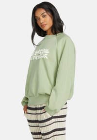 Lichtgroene sweatshirt met een wit bloemenpatroon, lange mouwen, ribbelmanchetten en een ribbelzoom. Gecombineerd met gestreepte gebreide broek met zwarte en crèmekleurige strepen.