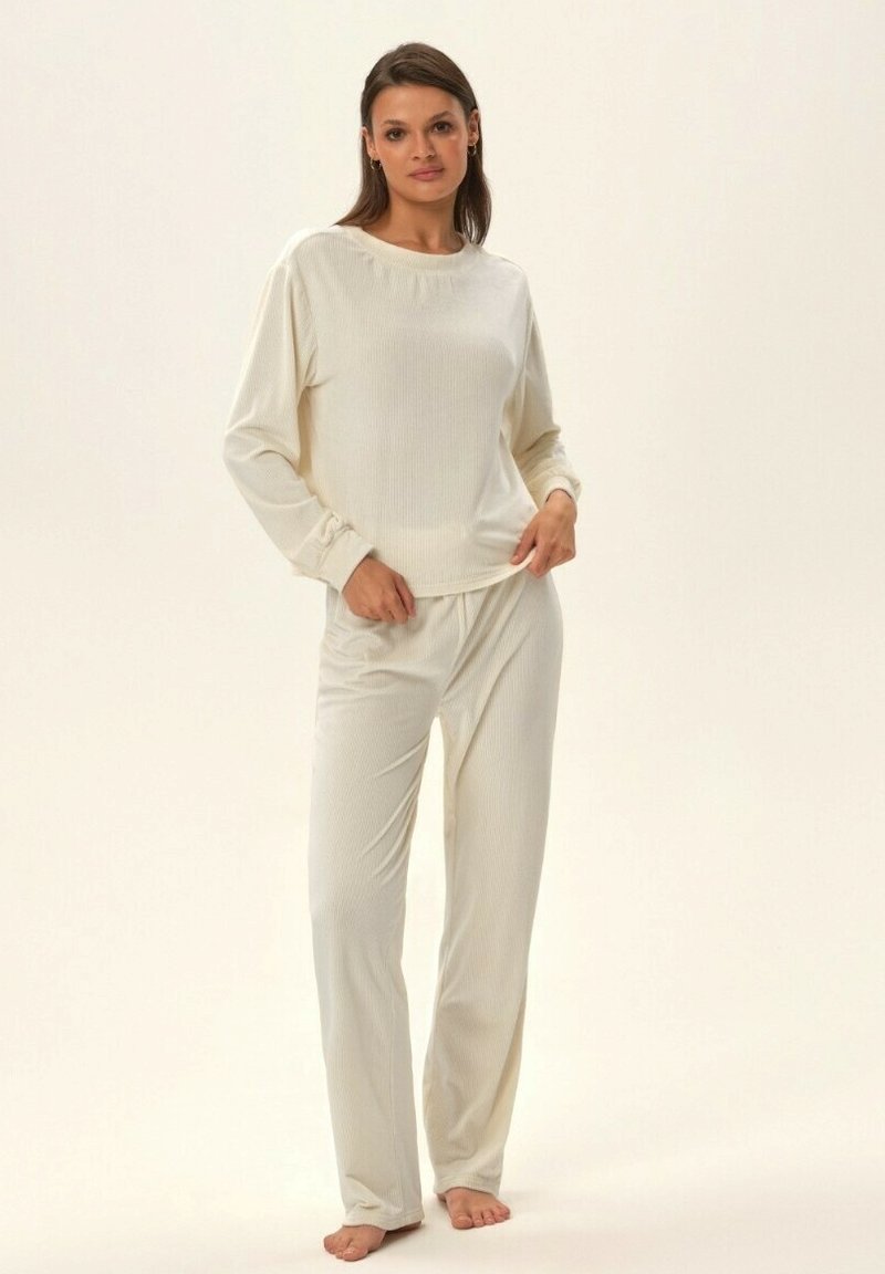 Kremowy, prążkowany top z długim rękawem i dopasowane spodnie z miękkiego materiału; posiada okrągły dekolt i dopasowane mankiety. Spodnie mają elastyczny pas.