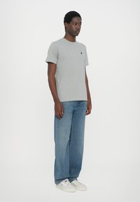 Tricou din bumbac gri, cu guler rotund, mâneci scurte și un mic logo. Asortat cu blugi denim evazați de culoare albastră deschisă și adidași albi.