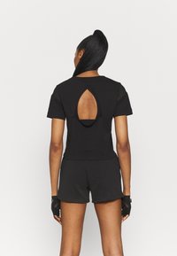 Černé sportovní triko s kulatým výstřihem a průřezem na zádech, krátké rukávy, nošené s černými šortkami a rukavicemi bez prstů.