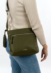 Olive green textured leather crossbody bag with a front zip pocket and a decorative tassel. Features a sleek design and adjustable strap.