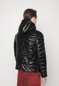 Černá péřová bunda s lesklou texturou, kapucí a geometrickým prošíváním. Má dlouhé rukávy a obepnutý střih.