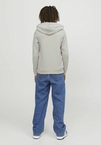 Felpa grigia chiara con un grande cappuccio, polsini e orlo a costine. Abbinata a jeans in denim blu a gamba larga e sneakers bianche.