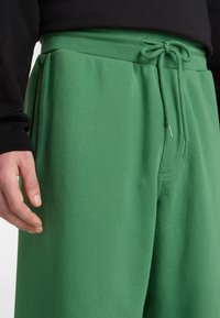 Groene sweatpants met een zachte textuur, voorzien van een verstelbare taille met koord en zijzakken. De stof lijkt elastisch en comfortabel.